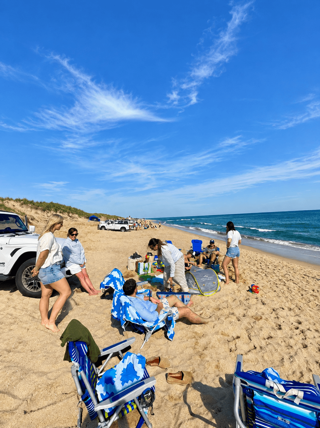 A group on the sand at Nobadeer Beach, with a Jeep parked by the dunes